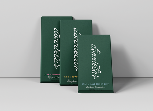 Three dark green rectangular boxes of 'dunnbear' Milk + Toasted Cereal Belgian Chocolate arranged in a staggered studio composition against a light gray background.