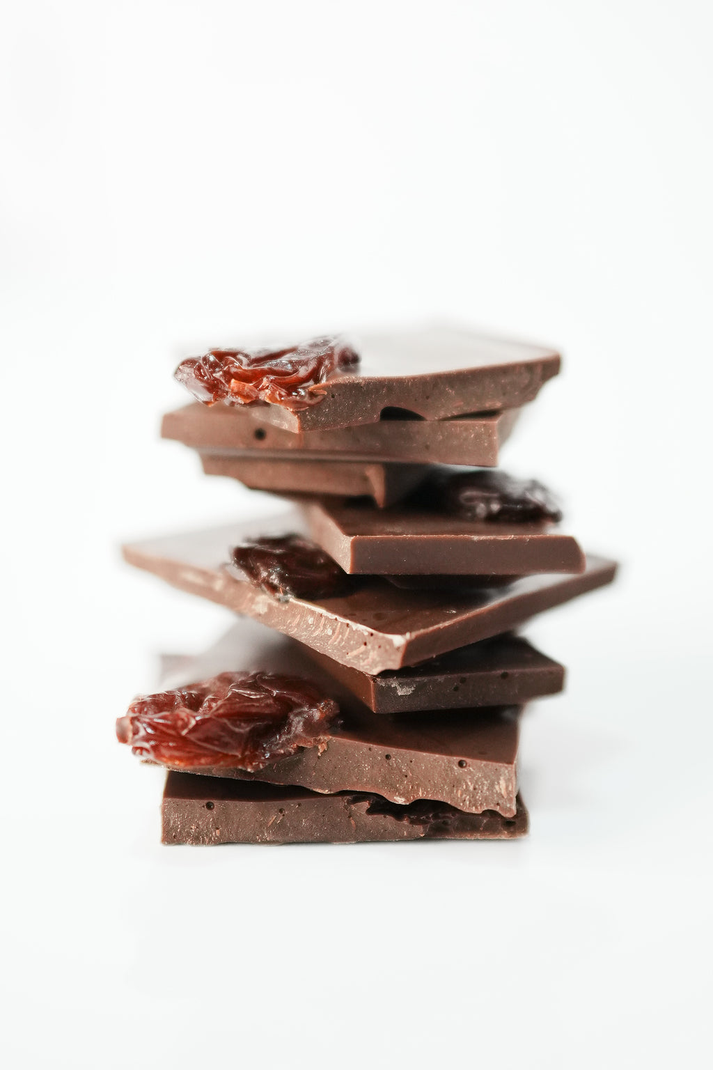 A stack of broken dark chocolate pieces with two pieces featuring dried fruit, set against a clean white background.