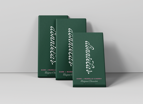 Three dark green rectangular chocolate boxes arranged in a fan shape on a light gray surface against a light gray background. The front box is labeled 'annueli' in white script, with 'DARK + MORELLO CHERRY' and 'Belgian Chocolate' printed below.