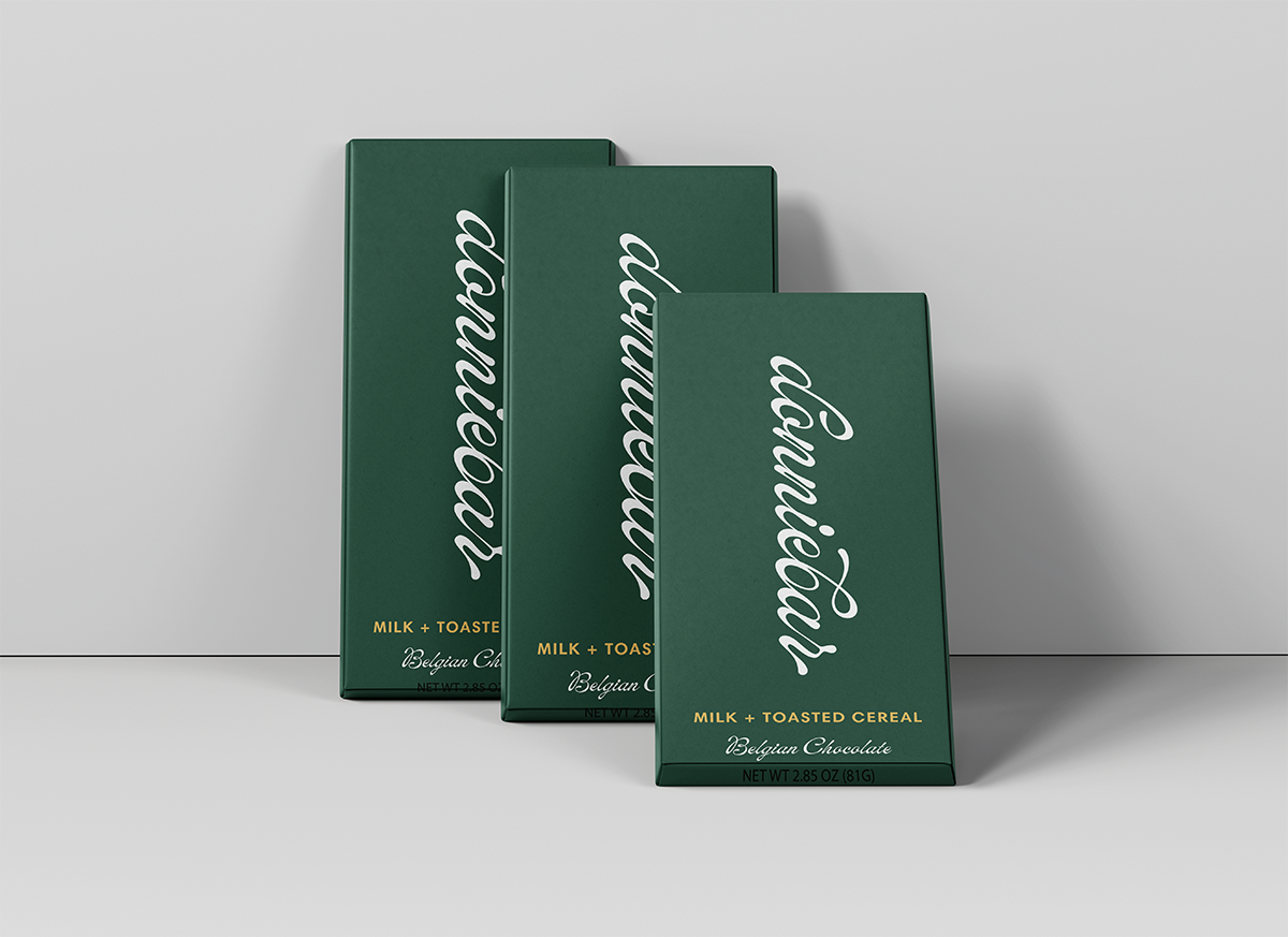 Three dark green rectangular boxes of 'dunnbear' Milk + Toasted Cereal Belgian Chocolate arranged in a staggered studio composition against a light gray background.