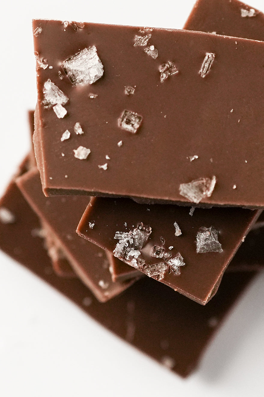 Close-up of stacked chocolate bars topped with coarse sea salt crystals on a white background.