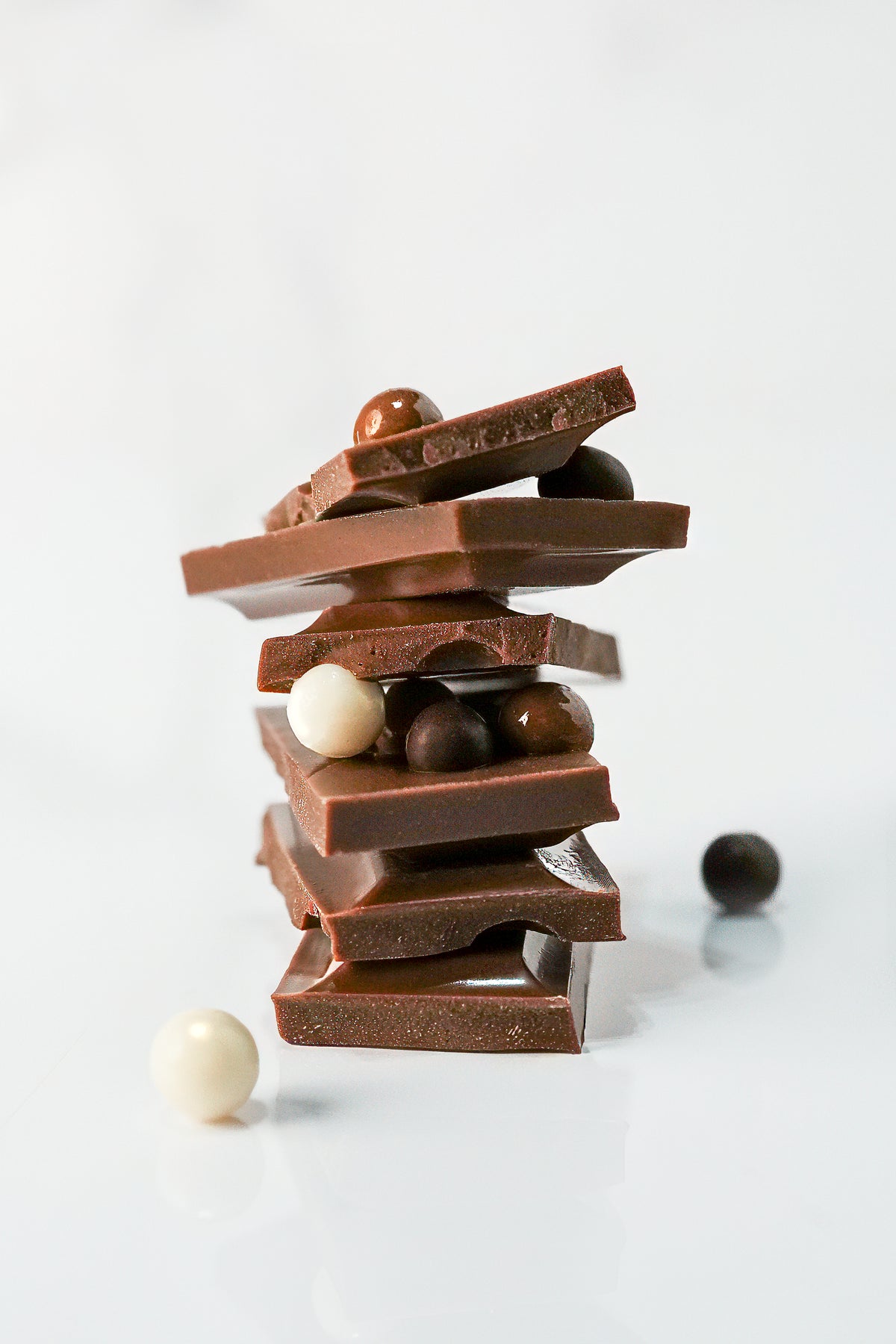 A stack of broken milk and dark chocolate bars with assorted chocolate candies, photographed on a clean white background.