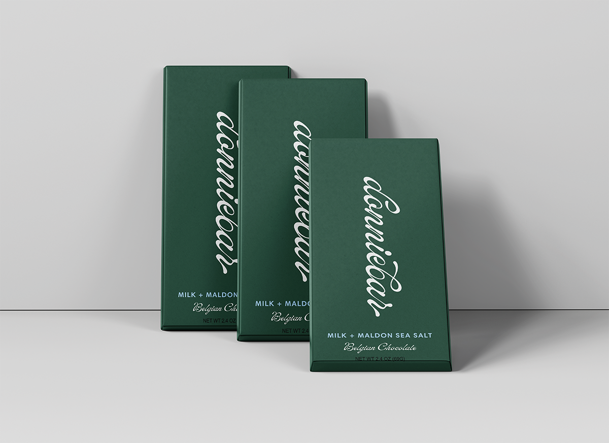 Three dark green rectangular chocolate boxes arranged in a staggered studio setup against a light gray background. The front box is slightly open, and all boxes feature large white cursive text reading 'conneault' with smaller white text below indicating milk and flavor details.