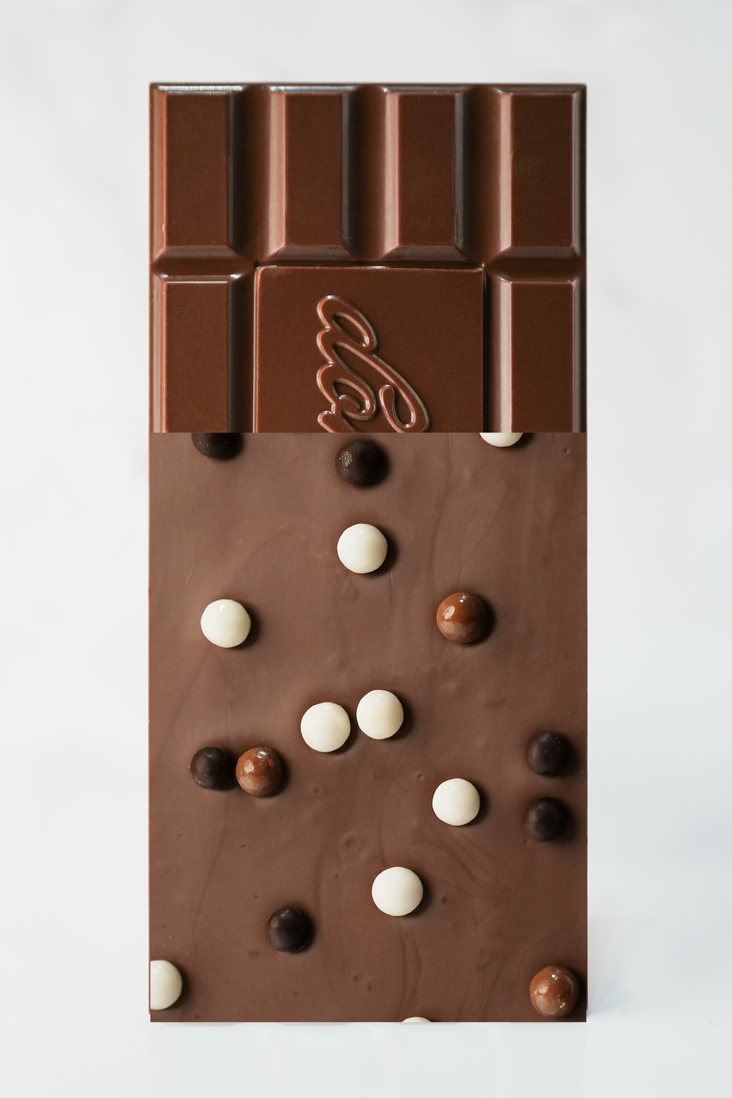 A chocolate bar with a glossy dark brown coating and scattered milk-chocolate and white candy-coated pieces, photographed from above on a plain white background.