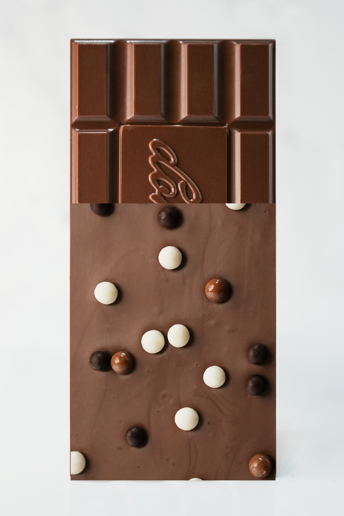 A chocolate bar with a glossy dark brown coating and scattered milk-chocolate and white candy-coated pieces, photographed from above on a plain white background.