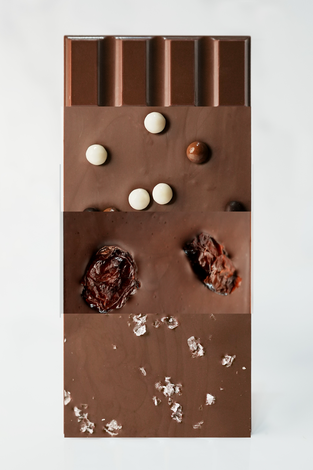 A vertical chocolate bar with a segmented top, decorated with white and milk chocolate candies, dark chocolate drizzle, and white chocolate flakes, set against a plain white background.
