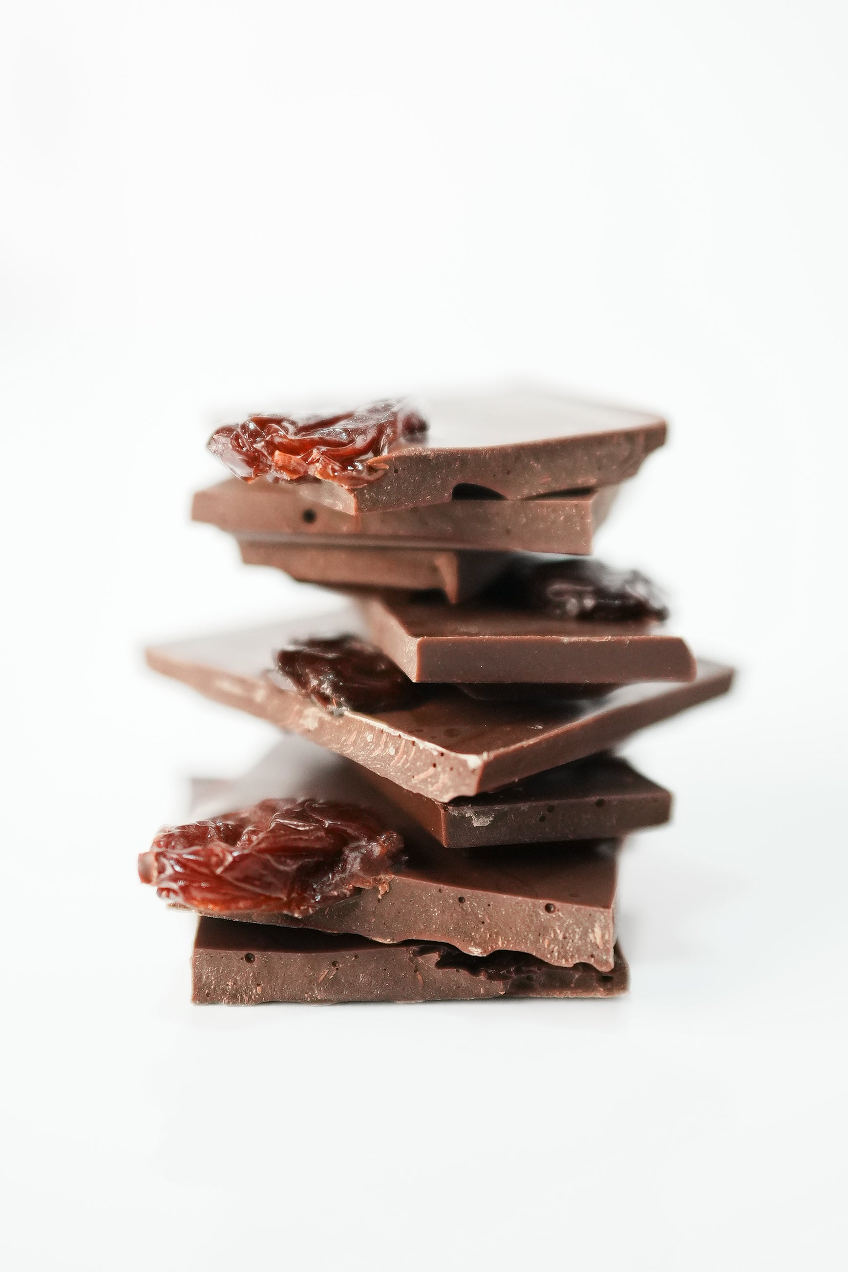A stack of broken dark chocolate pieces with two pieces featuring dried fruit, set against a clean white background.