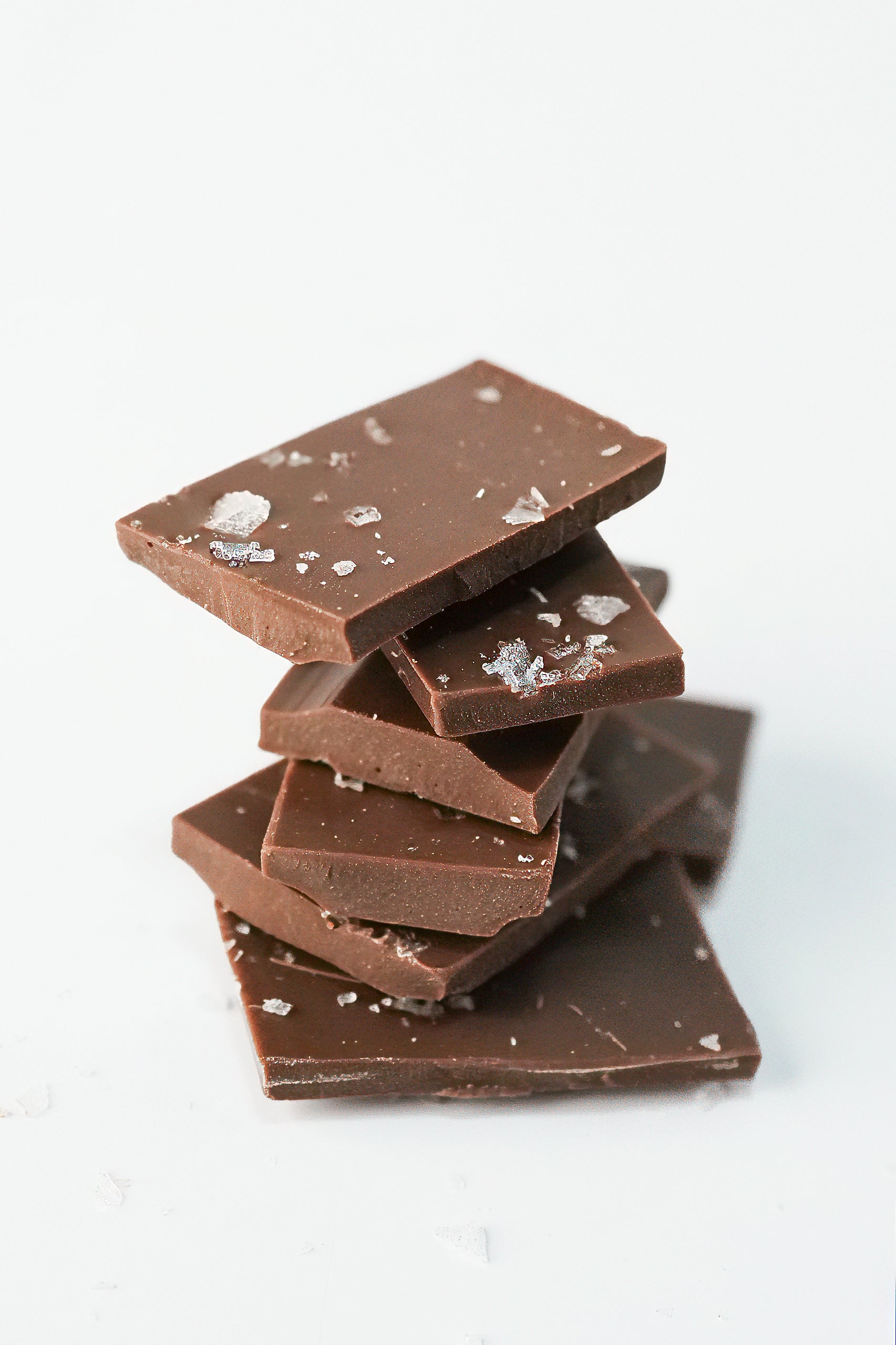 A stack of dark chocolate bars with coarse sea salt crystals, photographed on a clean white background.