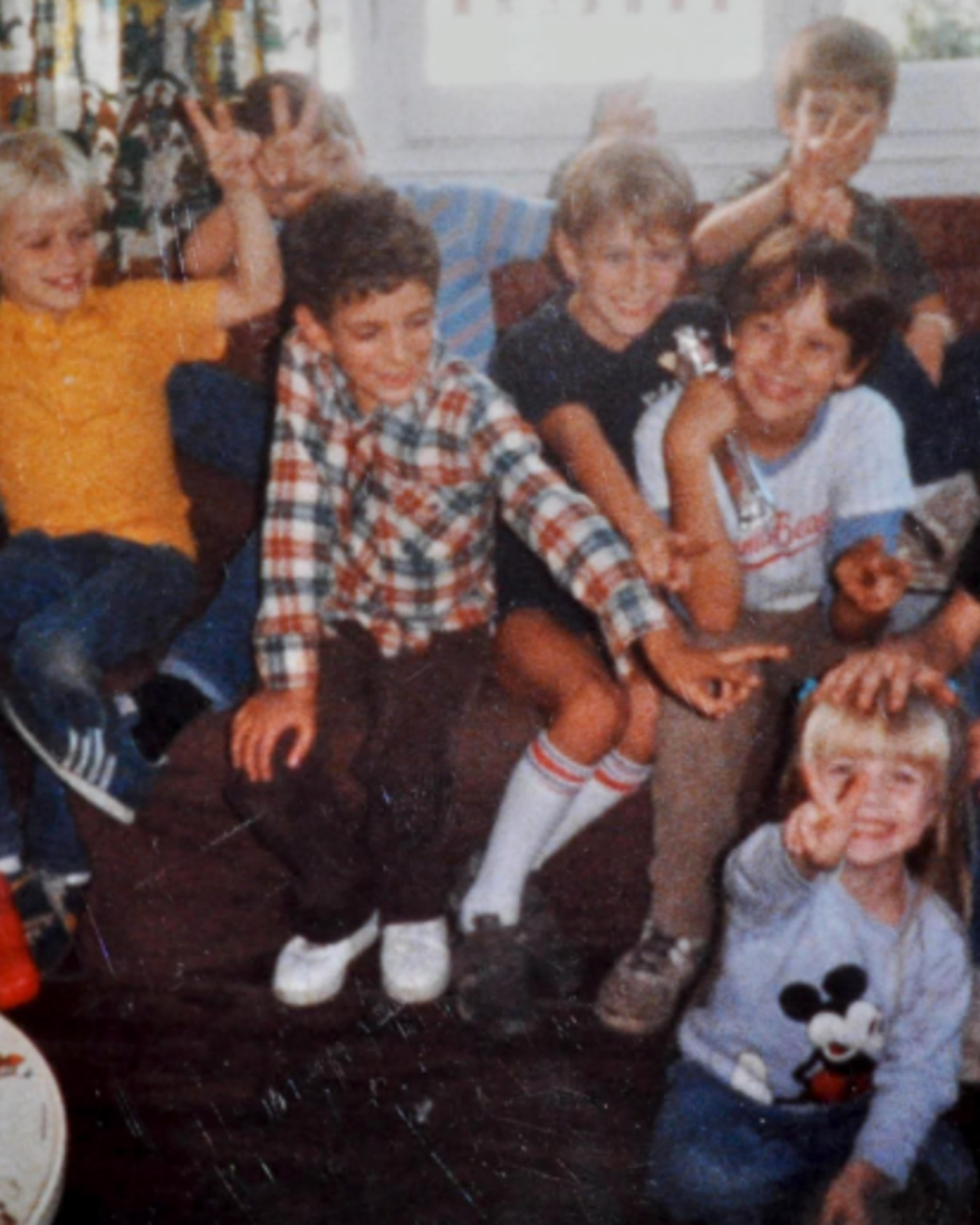 A group of children posing together in a cozy indoor setting, with one child in the foreground wearing a light blue Mickey Mouse t-shirt.